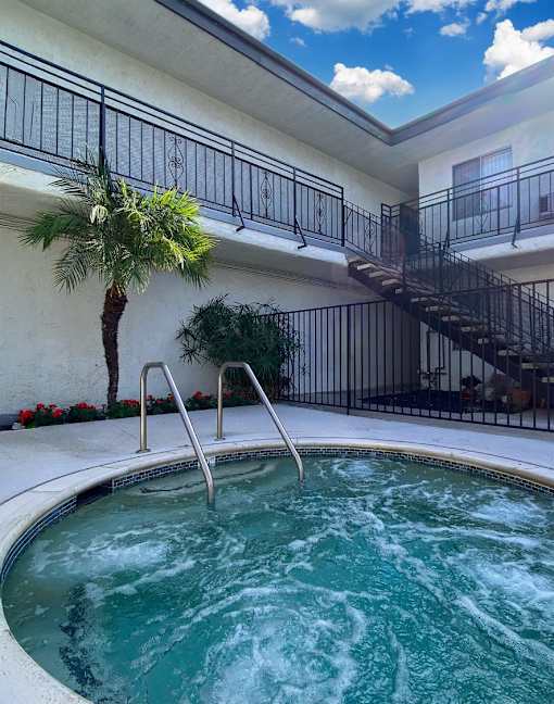 A hot tub sits in the middle of a patio with a staircase and a balcony in the background.