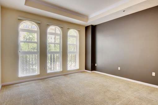 A room with a carpeted floor and three windows.