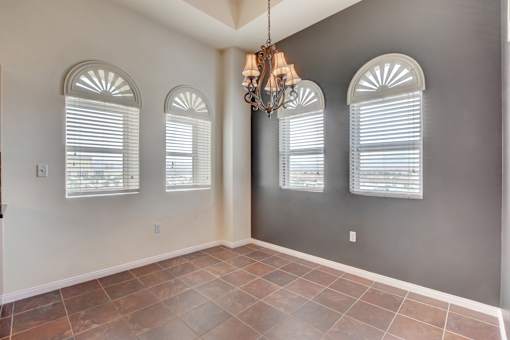 A room with a chandelier, arched windows, and tiled flooring.