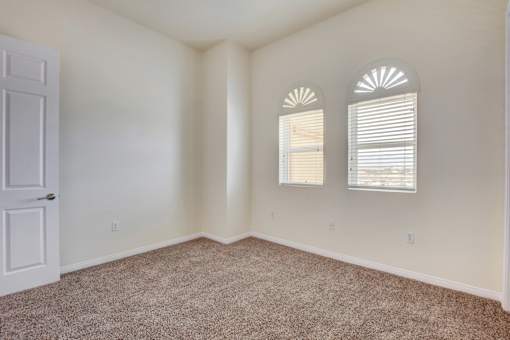 A room with a carpeted floor, a door, and two windows with blinds.