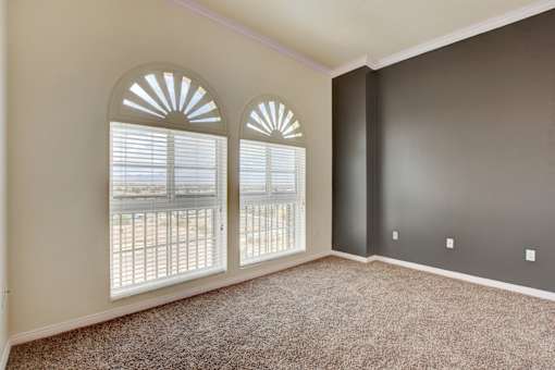 A room with carpeted floor and two windows with white blinds.