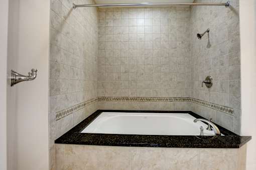 A bathroom with a black marble ledge and a white bathtub.