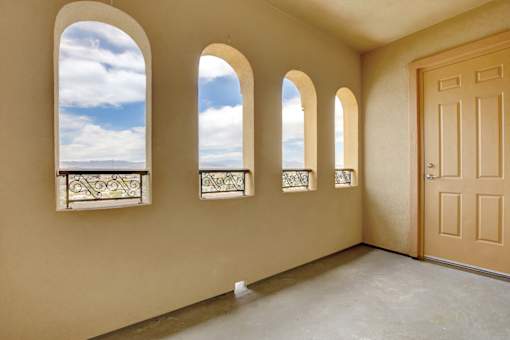 A room with a brown door and three windows with a view of the sky.