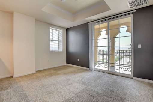 A room with a carpeted floor and a sliding glass door leading to a balcony.