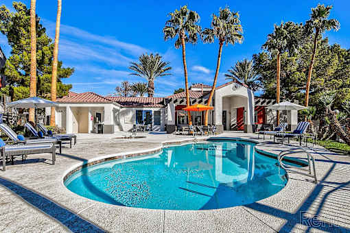 A pool surrounded by palm trees and lounge chairs.