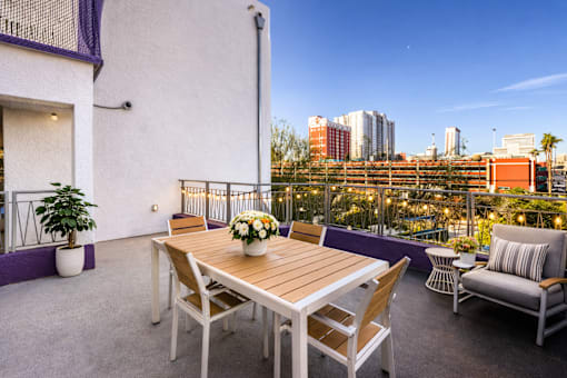 A table with chairs and a potted plant on a balcony overlooking a city.