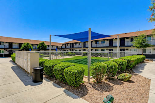 A sunny day at a residential complex with a blue shade structure and neatly trimmed bushes.