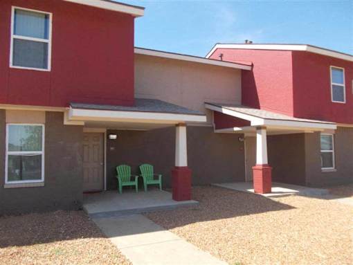 A red and beige house with a covered patio and two green chairs.