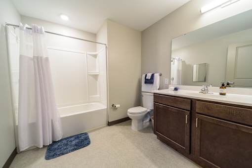 A bathroom with a white tub, a white toilet, a sink, and a blue rug.