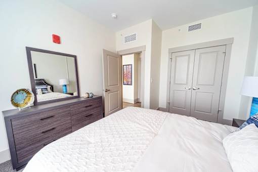 A bedroom with a large bed, a dresser with a mirror, and a doorway leading to another room.