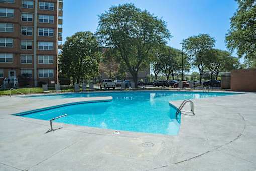 A swimming pool surrounded by trees and a building in the background.
