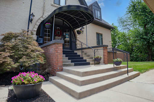 A house with a black awning and a brick pillar with steps leading up to the door.