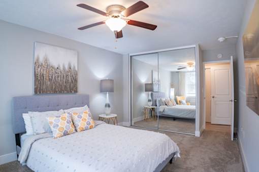 A bedroom with a bed, a ceiling fan, and a painting on the wall.