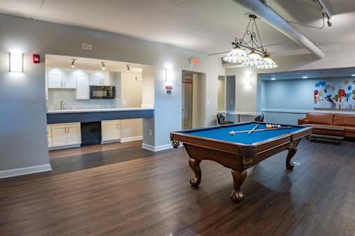 A pool table is in the middle of a room with a bar and a television.