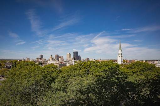 A cityscape with a church steeple stands out against a backdrop of buildings and trees.