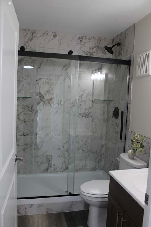 A white toilet sits in a marble bathroom next to a walk-in shower.