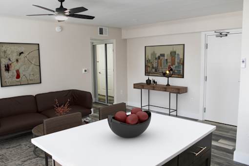 A living room with a brown couch, a white table, and a ceiling fan.