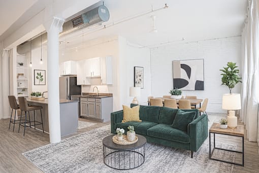A living room with a green couch and a grey kitchen in the background.