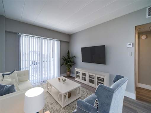A living room with a white couch, a blue chair, and a television mounted on the wall.