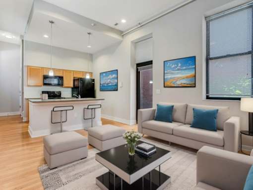 A modern living room with a kitchen area in the background.
