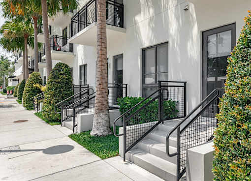 A white building with black railings and a palm tree in front.