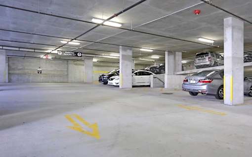 A parking garage with cars parked and a yellow arrow on the ground.
