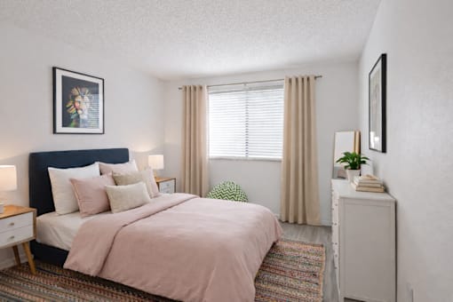 A bedroom with a bed, nightstand, and a window with curtains.