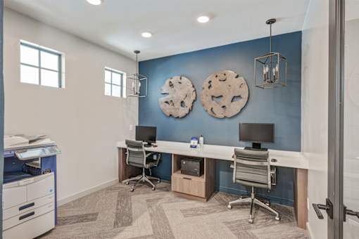 A room with a blue wall and a white desk with two monitors.