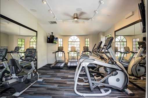 A gym with treadmills, elliptical machines, and a fan.