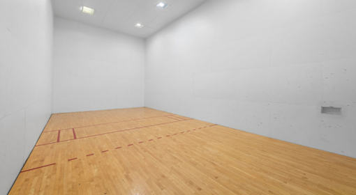 A squash court with a wooden floor and white walls.