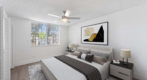 A bedroom with a large bed, a ceiling fan, and a painting on the wall.