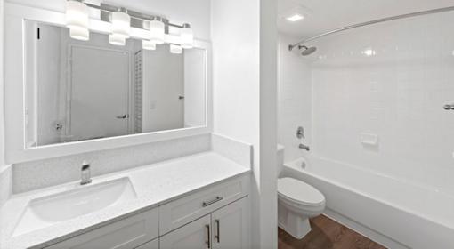 A white bathroom with a sink, mirror, toilet and bathtub.