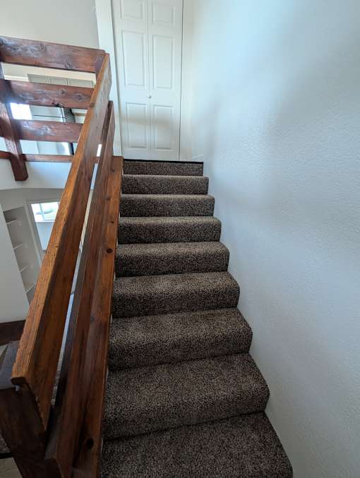 A staircase with a wooden handrail and a carpeted runner.