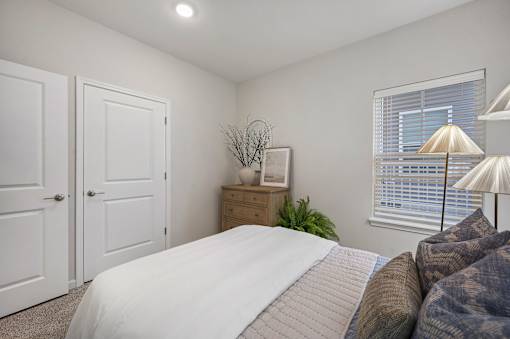 A bedroom with a bed, a nightstand, and a window with blinds.