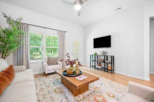 A living room with a white couch, a coffee table, and a flat screen TV mounted on the wall.