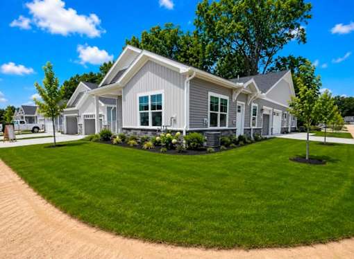 A house with a grey roof and white walls is surrounded by a well-manicured lawn.