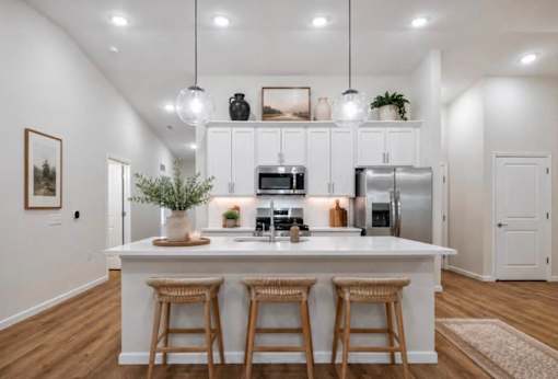 A kitchen with white cabinets and a white island with three bar stools.