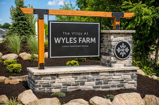 A sign for The Villas at Wyles Farm, a luxury apartment complex, is displayed in a landscaped area.