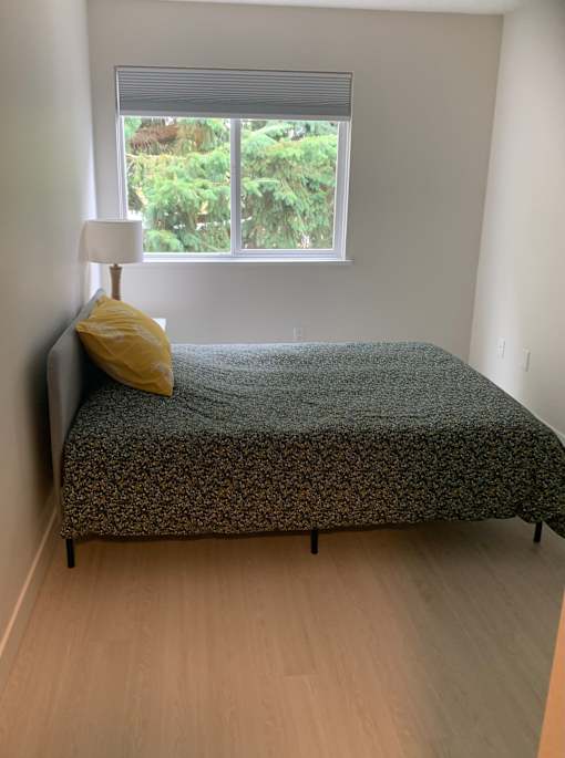 A bed with a yellow pillow and a grey blanket in a room with a window.