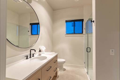 A bathroom with a white counter top and a round mirror.