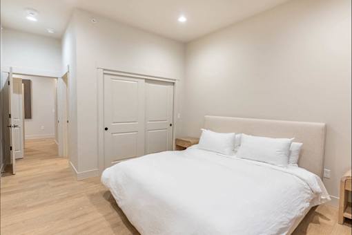 A white bed with a white headboard and two white pillows in a bedroom with wooden floors and white walls.