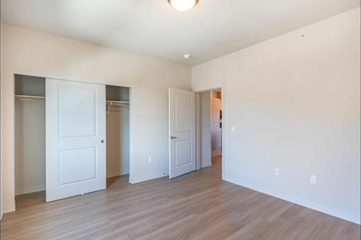 A room with white walls and wooden flooring with three white doors.
