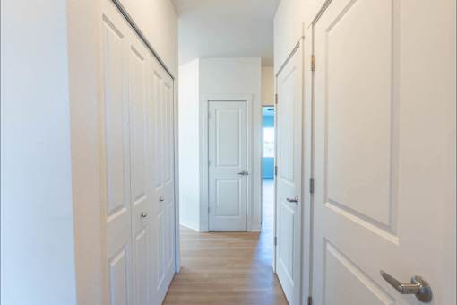 A long hallway with white doors and a wooden floor.