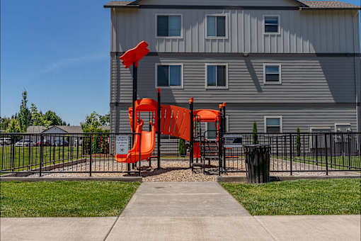 A playground with a slide and a building in the background.