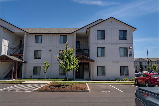 A white apartment building with a red car parked in front.