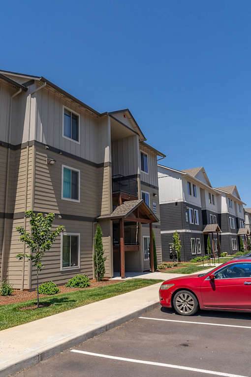 A red car is parked in a parking lot in front of a building.