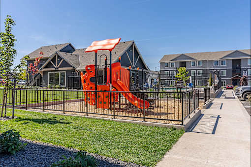 A playground with a red slide is in front of a building at Cascade Place Apartment Homes, Molalla, 97038