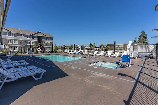 A pool area with sun loungers and a building in the background at Cascade Place Apartment Homes, Molalla, OR, 97038
