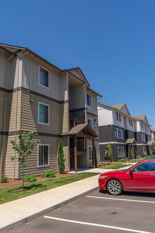 A red car is parked in a parking lot in front of a building at Northplace Apartment Homes, Salem
