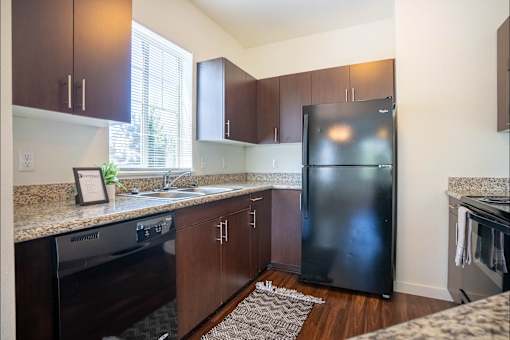 A kitchen with a black fridge and wooden cabinets at Riverplace Apartment Homes, Independence